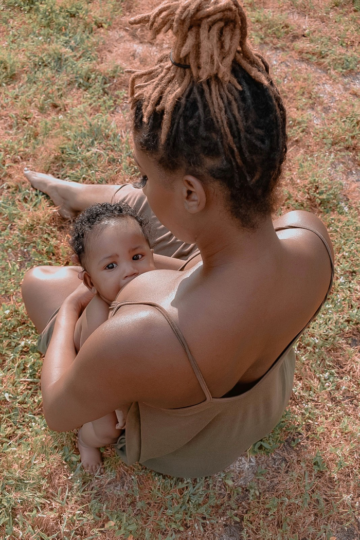 A tender moment of a mother breastfeeding her baby while sitting outside on a sunny day.
