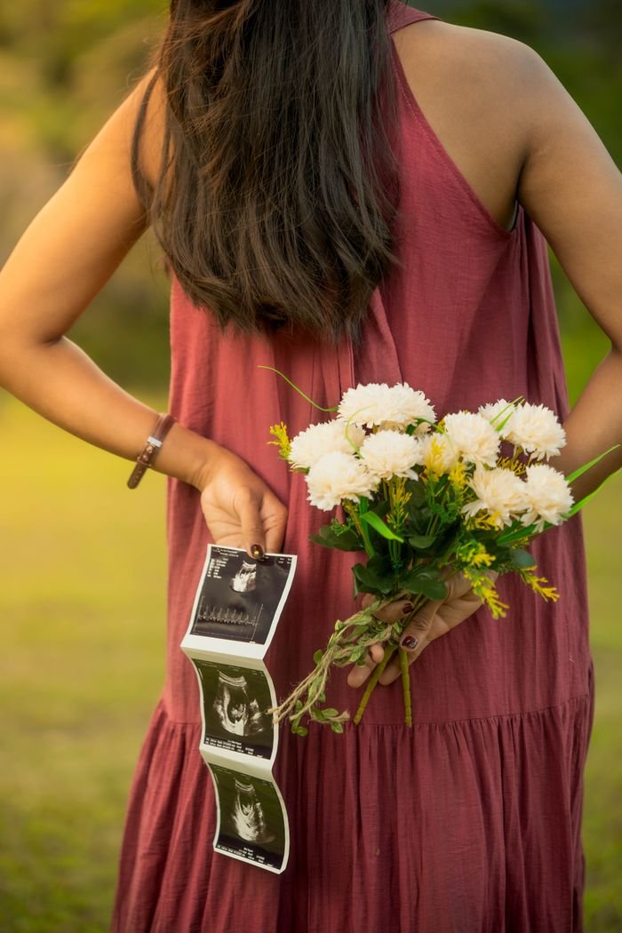 Pregnant woman holding flowers and ultrasound photos in a serene outdoor setting.