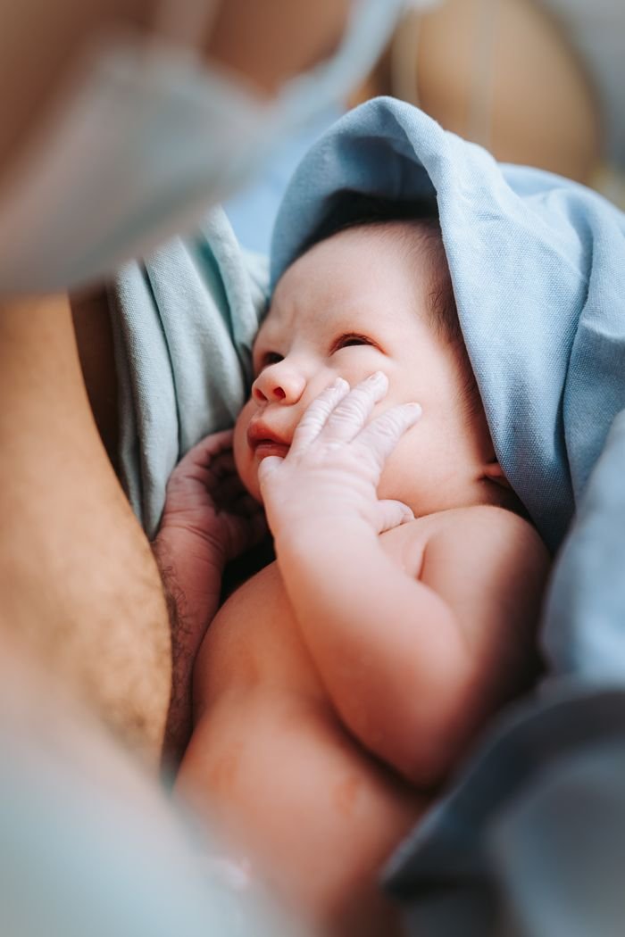 Tender moment of a newborn baby wrapped in a blue blanket, gazing lovingly at a parent.