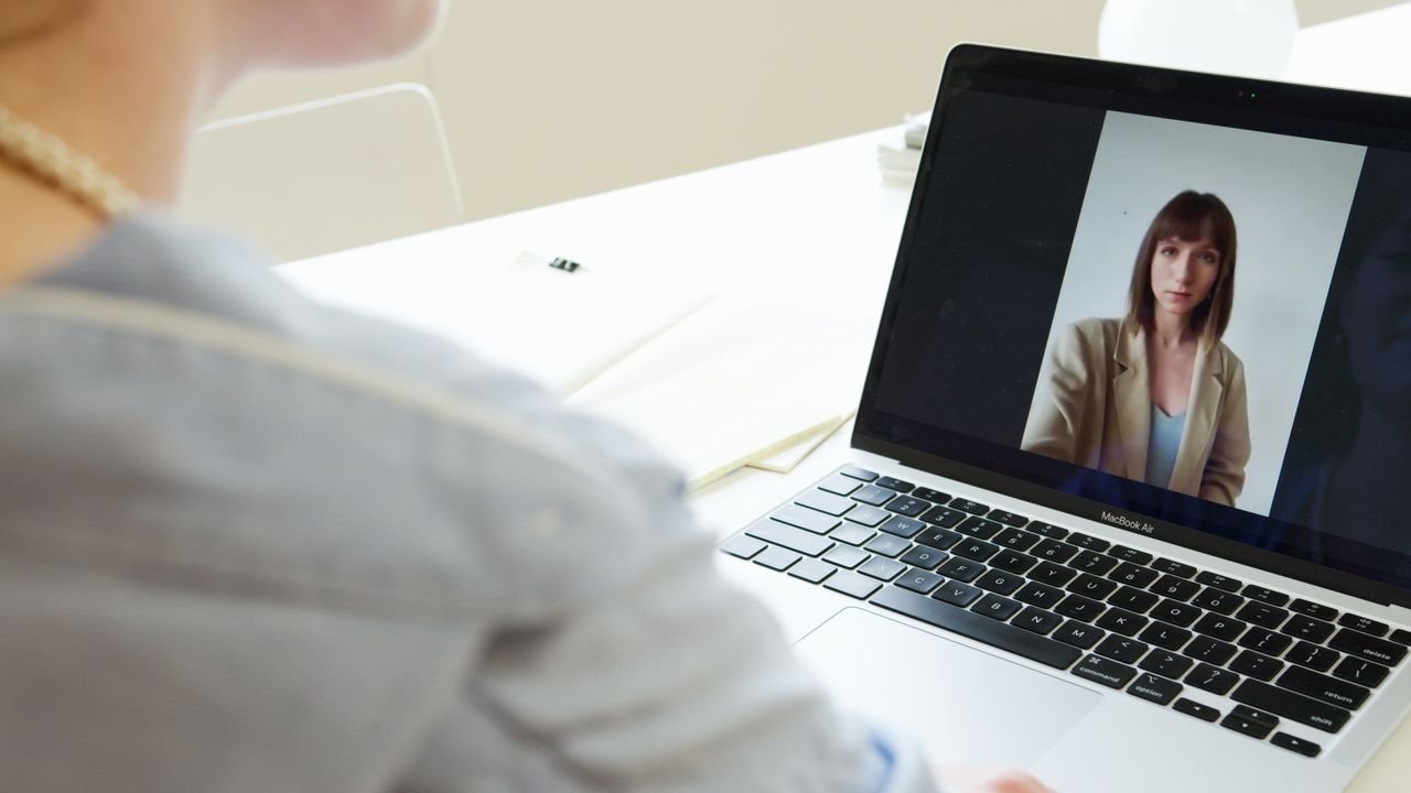 Close-up of woman on a video call using a laptop in a modern workspace.
